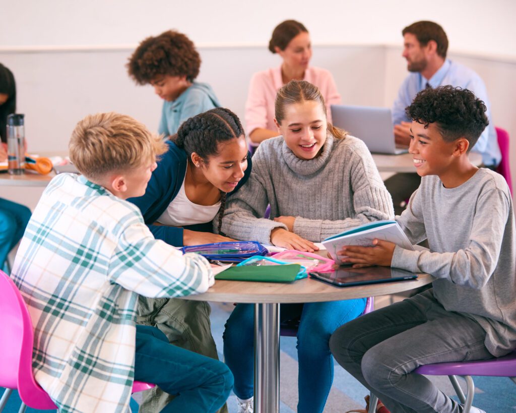 Secondary Or High School Students Collaborating In Study Area With Teachers In Background