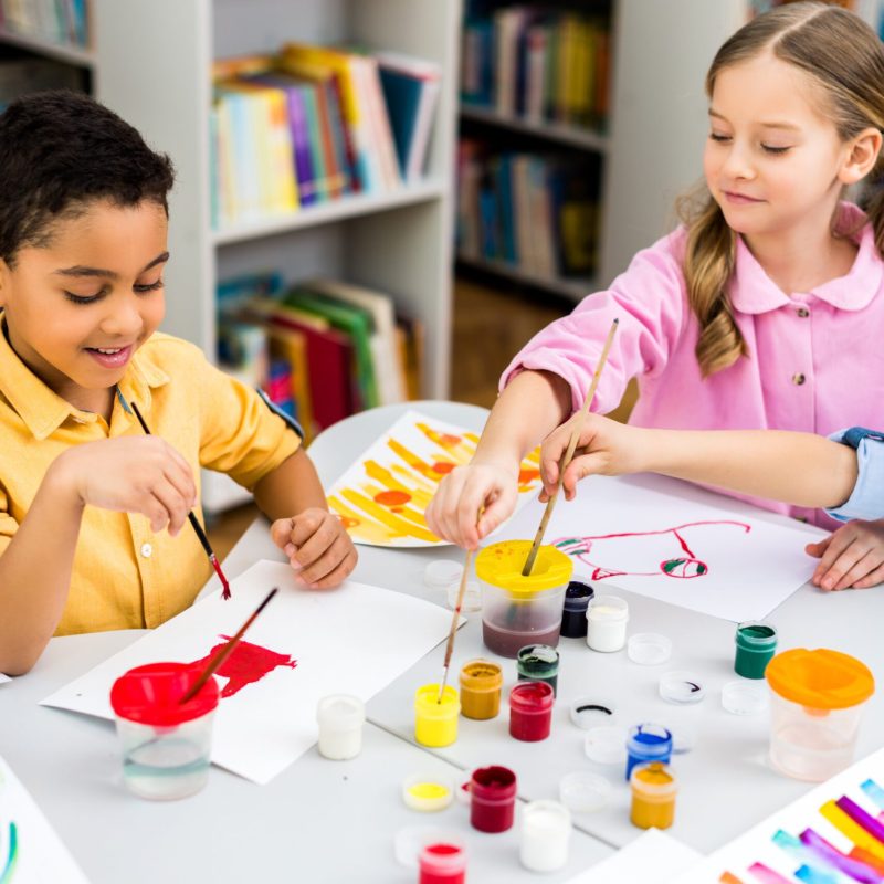 selective focus of happy multicultural kids painting on papers